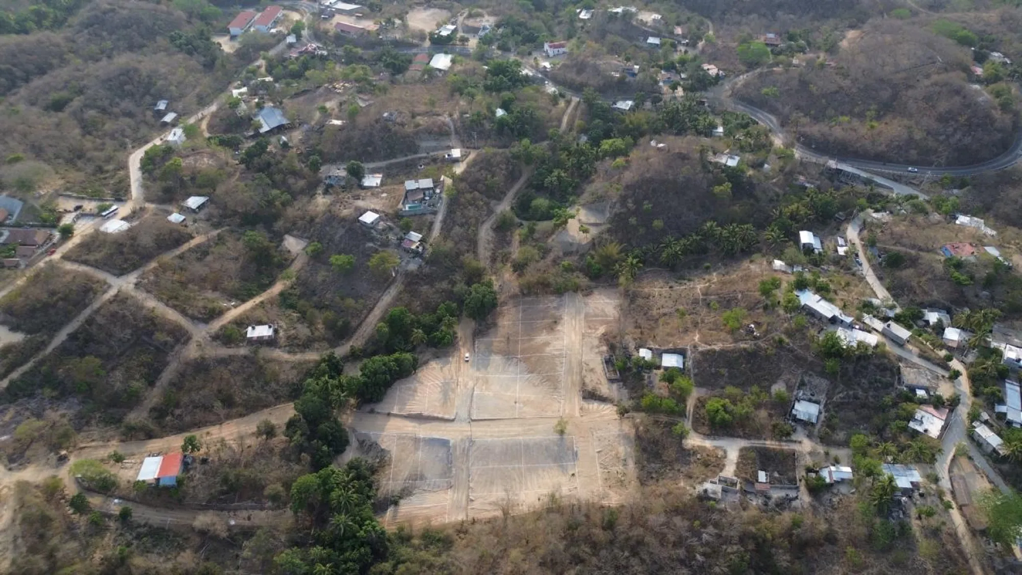 Vista aérea de un claro de tierra clara entre cerros secos y casas dispersas
