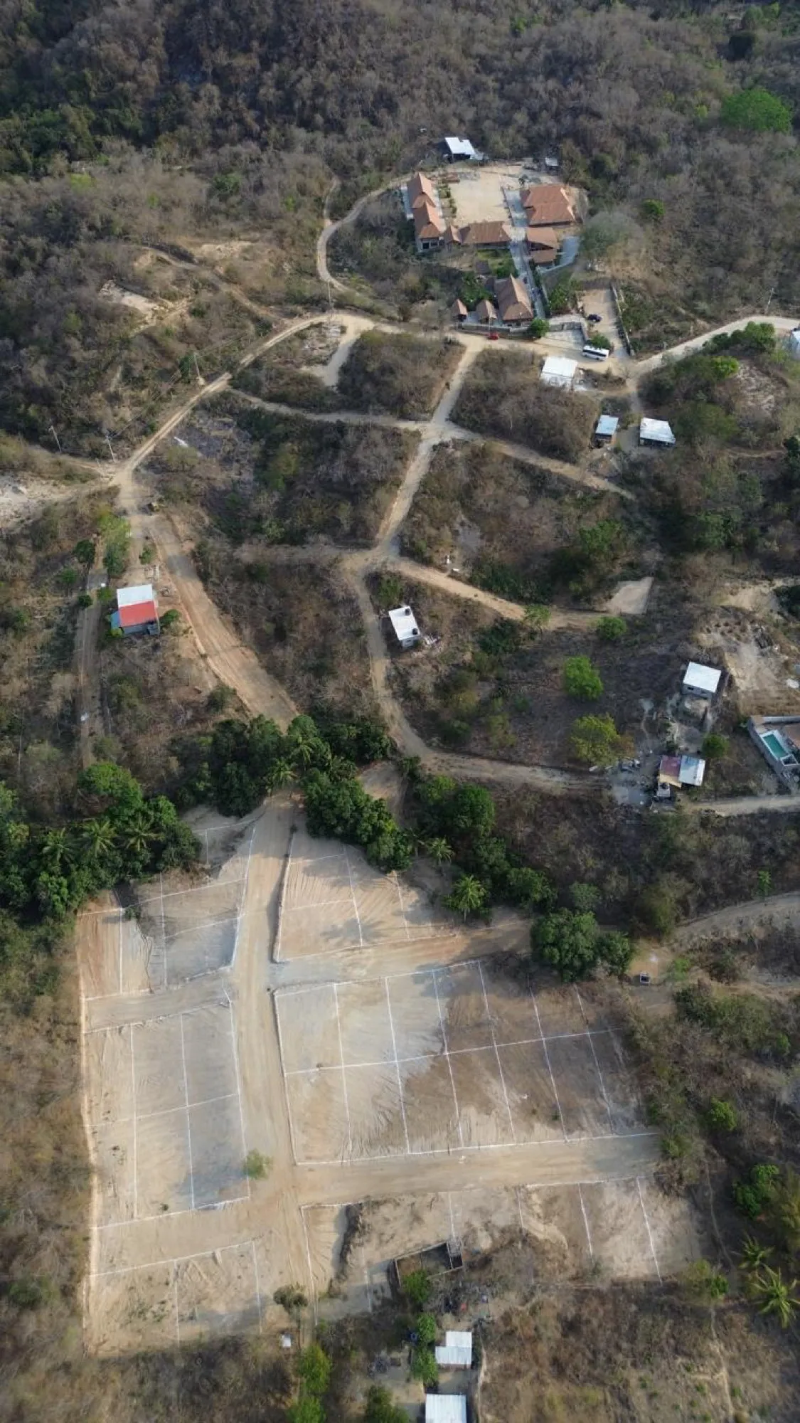 Vista aérea de un claro de tierra con trazos y caminos entre cerros secos y construcciones pequeñas