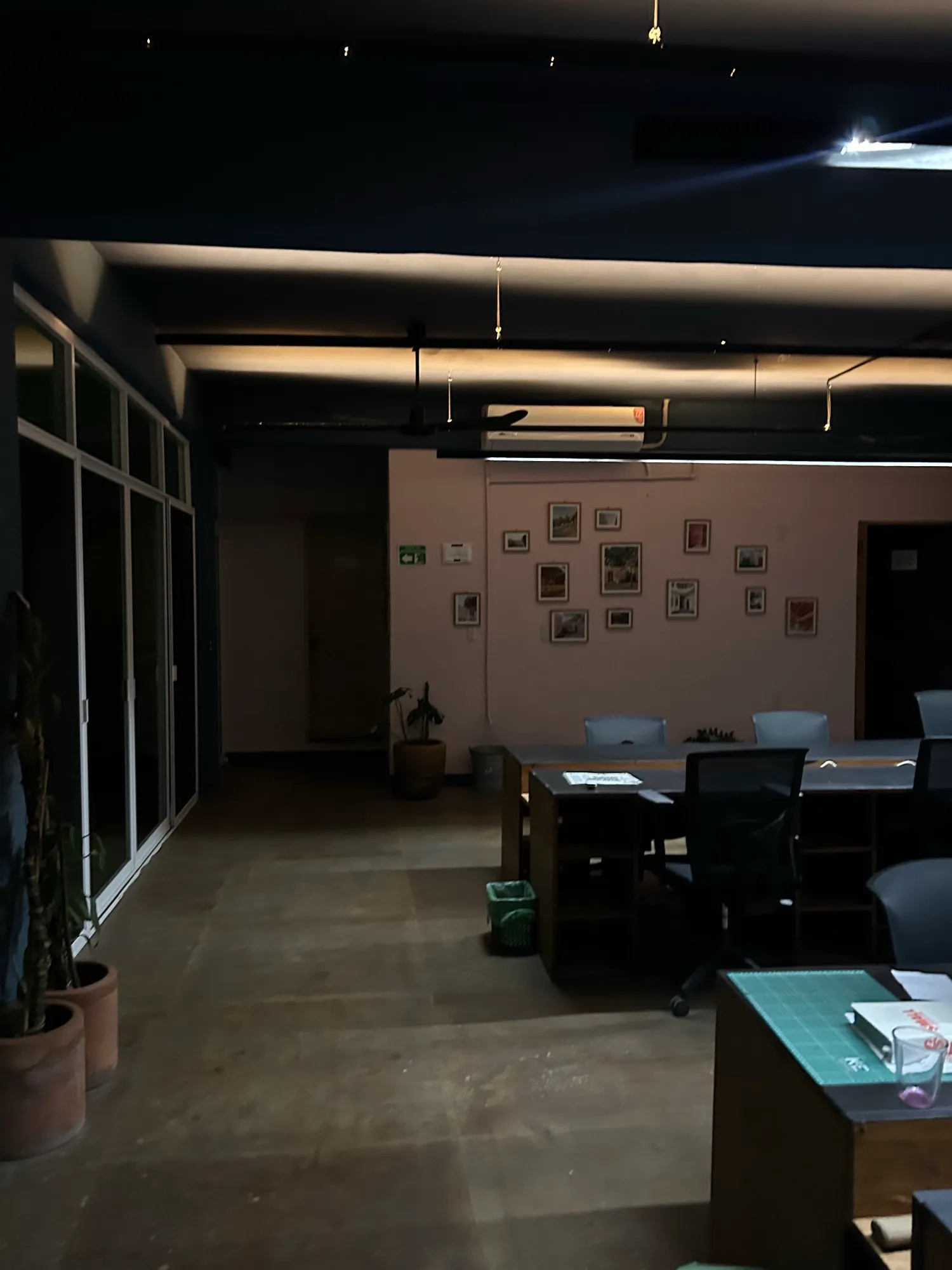 Oficina con plantas, ventanales a la izquierda y escritorios al fondo